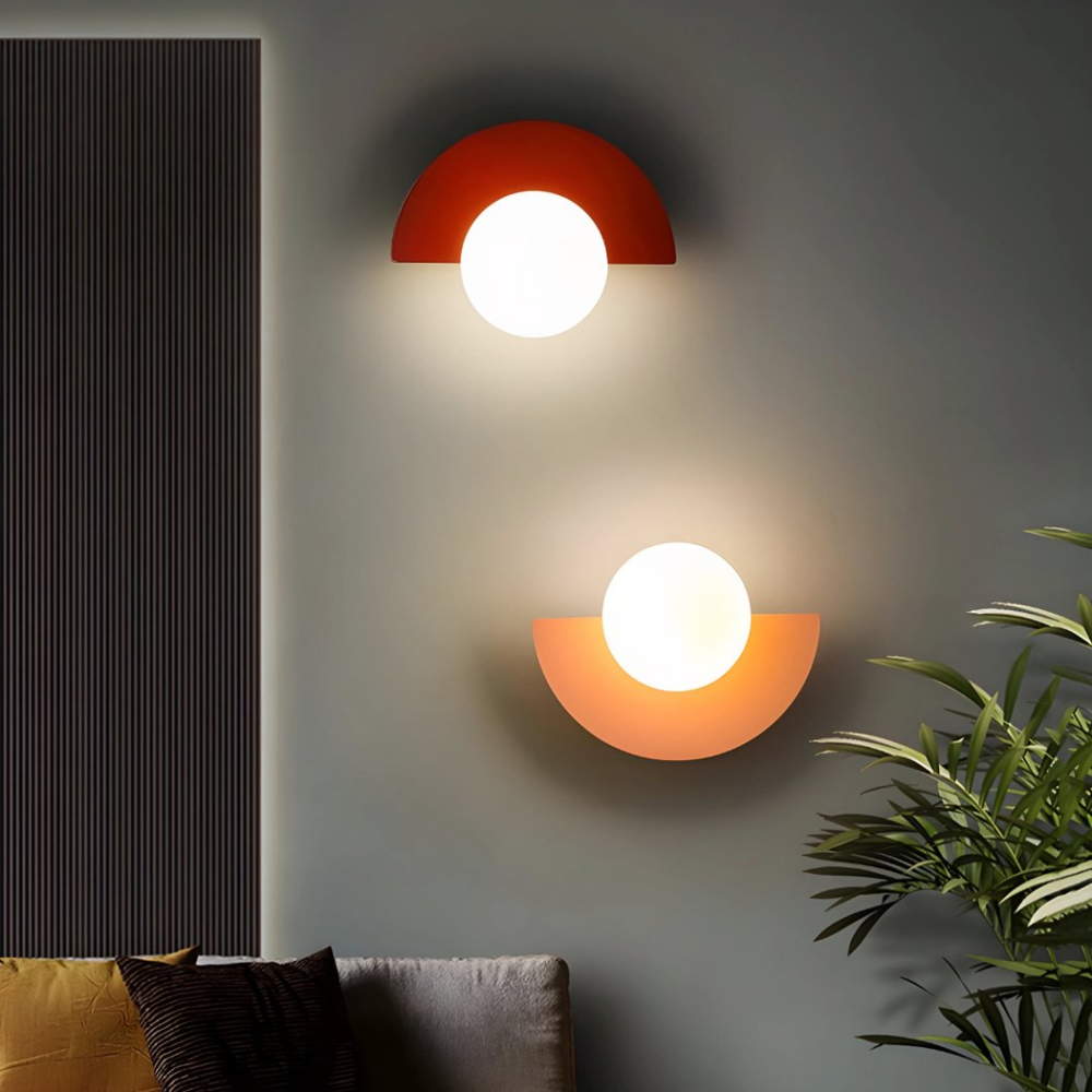 Deux appliques murales en demi-lune style rétro et colorées en rouge et rose sont accrochées sur un mur à côté d'une plante d'intérieur