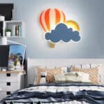 Lampe murale en forme de montgolfière et de nuage accroché à un mur au-dessus d'un lit dans une chambre d'enfant