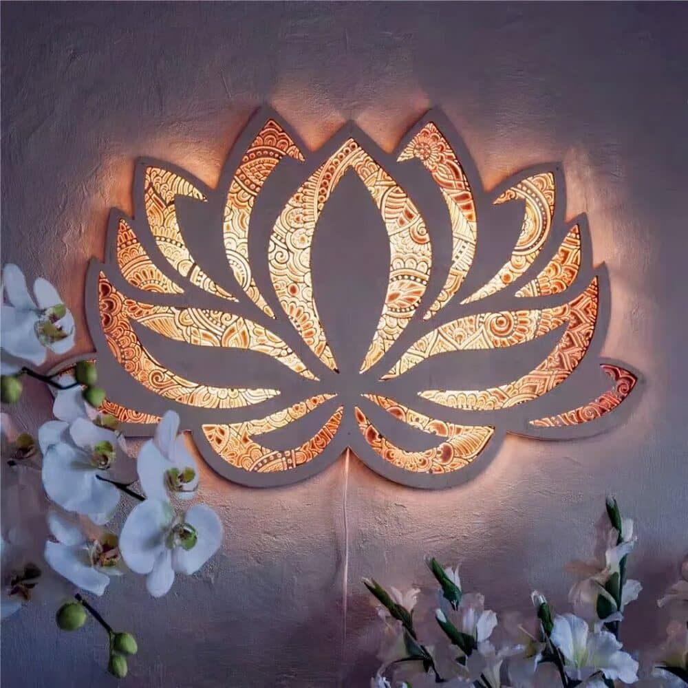 Applique murale fleur de lotus style mandala allumée, laissant passer la lumière à travers ses motifs ajourés. Des fleurs style géranium sont visibles dans les angles en bas de l'image.