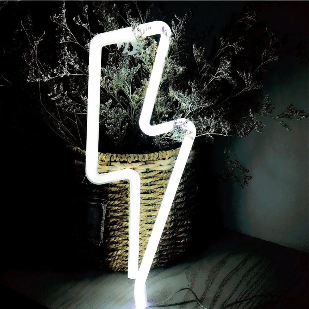 Applique néon LED en forme d'éclair de lumière blanche, posé sur une table et contre une plante.