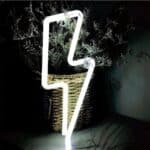 Applique néon LED en forme d'éclair de lumière blanche, posé sur une table et contre une plante.
