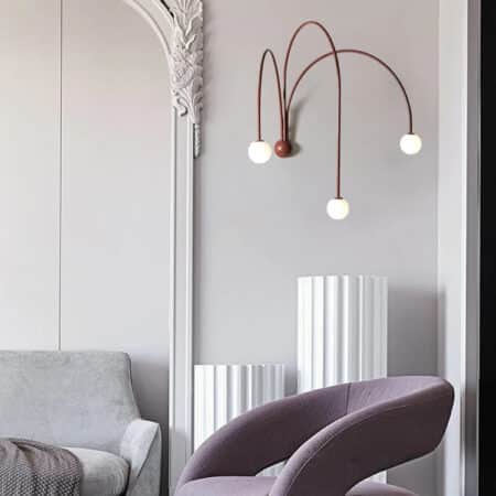 Applique murale design salon couleur terracotta allumée et fixée sur un mur blanc dans un salon, à côté d'un canapé.