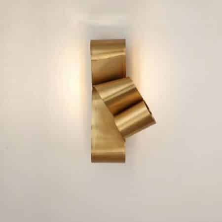 on voit sur un mur clair une applique murale dorée en forme de ruban