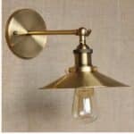 on voit sur un mur marron clair une applique murale dorée de style industriel à abat-jour plat