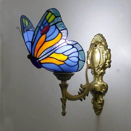 on voit posée sur un mur gris clair une applique murale de style Tiffany en forme de papillon de couleur bleu