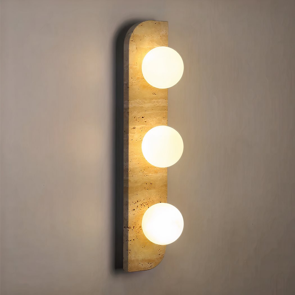 Applique murale de forme rectangulaire arrondie sur 2 angles opposés, en pierre de couleur beige, avec 3 boules lumineuses allumées. Fixée à la verticale sur un mur marron clair.