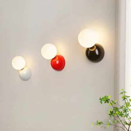 on voit sur un mur gris clair 3 appliques murales en forme de boule pour tête de lit de trois couleurs différentes, une blanche, une rouge et une noire
