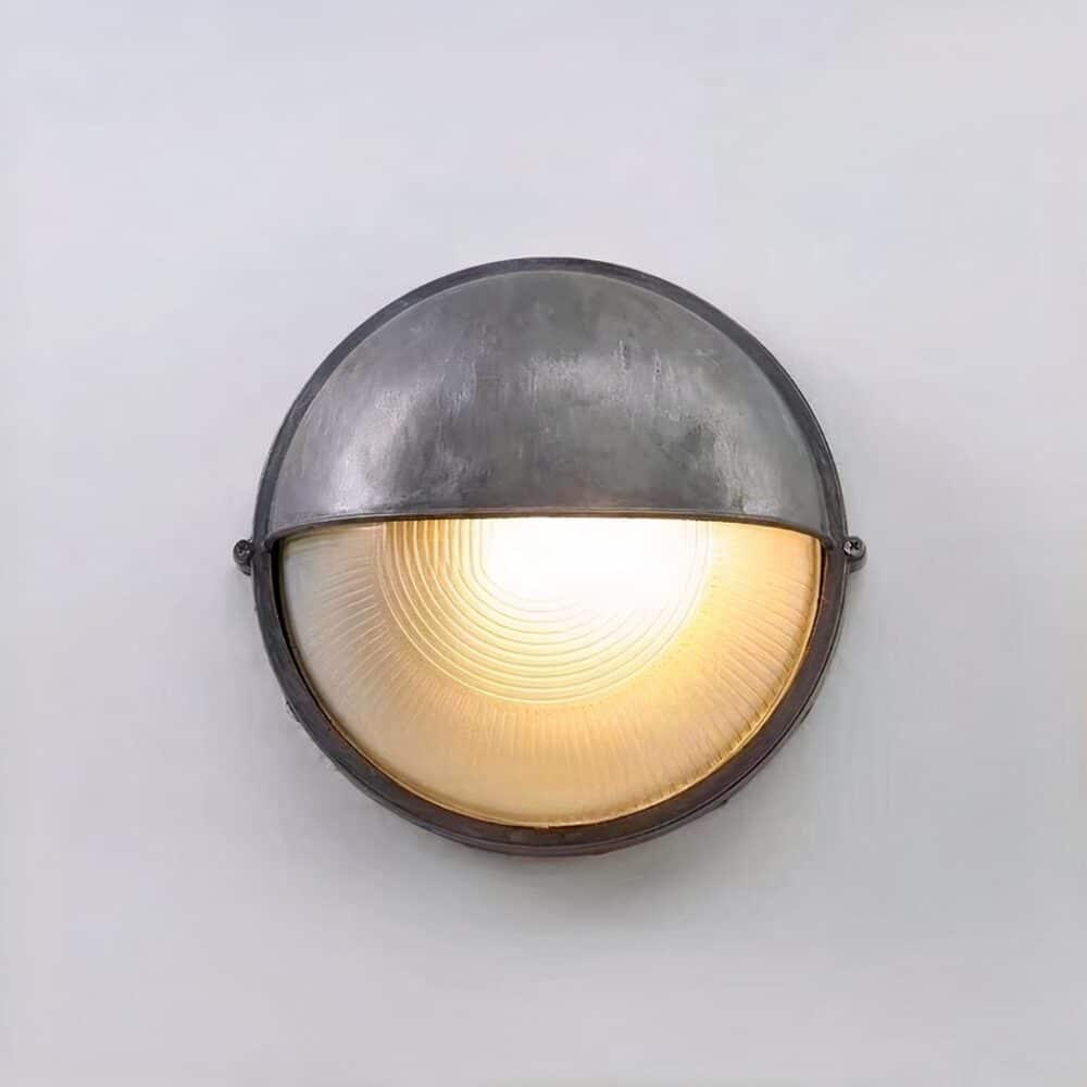 on voit sur un mur gris clair une applique murale dans le style industriel vissé contre le mur