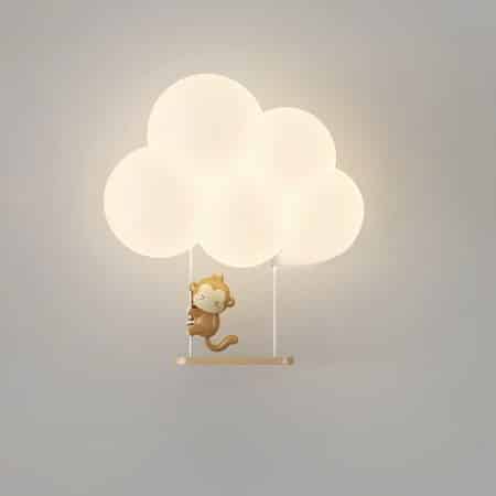 Applique murale en forme de nuage allumée avec une balançoire en-dessous et un petit singe de dessin animé accroché sur la ficelle de gauche. L'applique est fixée sur un mur gris.