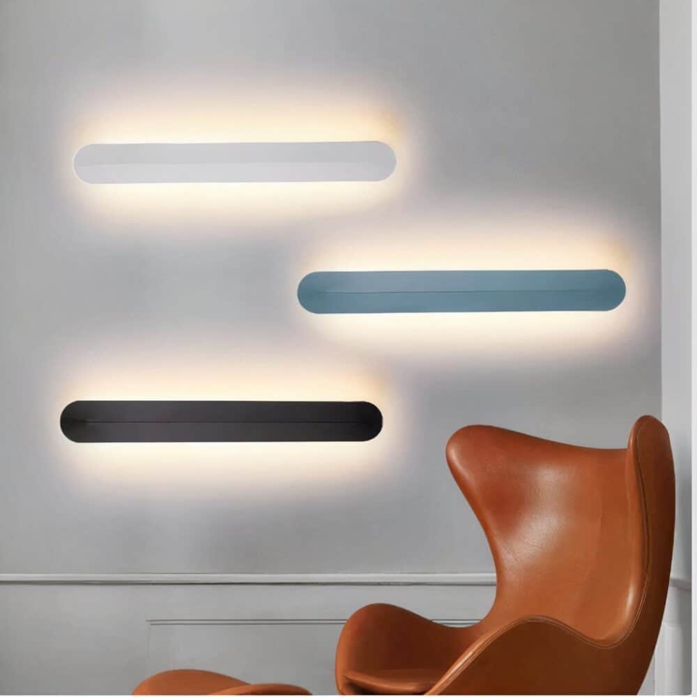 Applique murale moderne design minimaliste dans ses trois versions, blanche noire et bleu canard, accrochées sur un mur à côté d'un fauteuil à oreilles en cuir cognac.