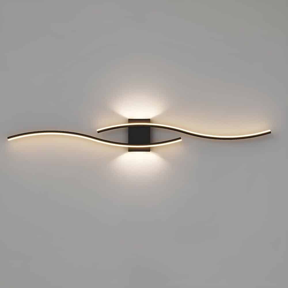 Applique murale noire fixée sur un mur gris, ayant la forme de 2 vagues l'une au-dessus de l'autre tenues par un support rectangulaire noire. Les vagues sont lumineuses et la lumière sort aussi du dessus et du dessous du support.