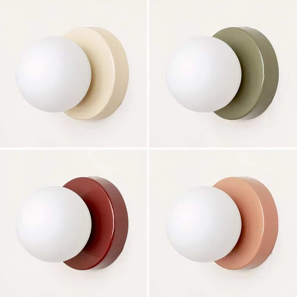 on voit 4 appliques murales en boule de 4 couleurs différentes rouge rose vert et blanc sur un mur blanc