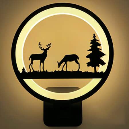 Applique murale ronde avec cercle lumineux. Le contour est noir et l'intérieur est lumineux. Au centre du cercle, un décor d'animaux avec un renne, une biche et un sapin, le tout en noir.