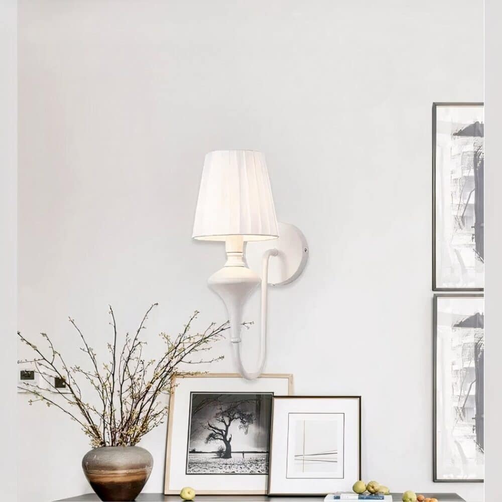 Applique murale en fer forgé et tissu blanc accrochée sur un mur blanc dans un salon, au-dessus d'un meuble.