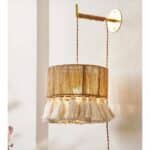 on voit dans une pièce aux murs clairs une applique murale en osier et à franges dans le style bohème