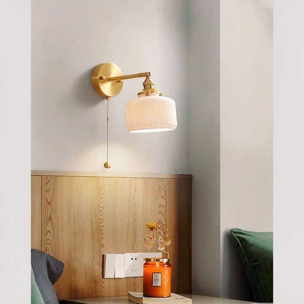 Applique murale rétro en céramique avec chainette d’allumage, dans sa version globe carré aux angles arrondis, allumée et fixée sur le mur d'une chambre à coucher.